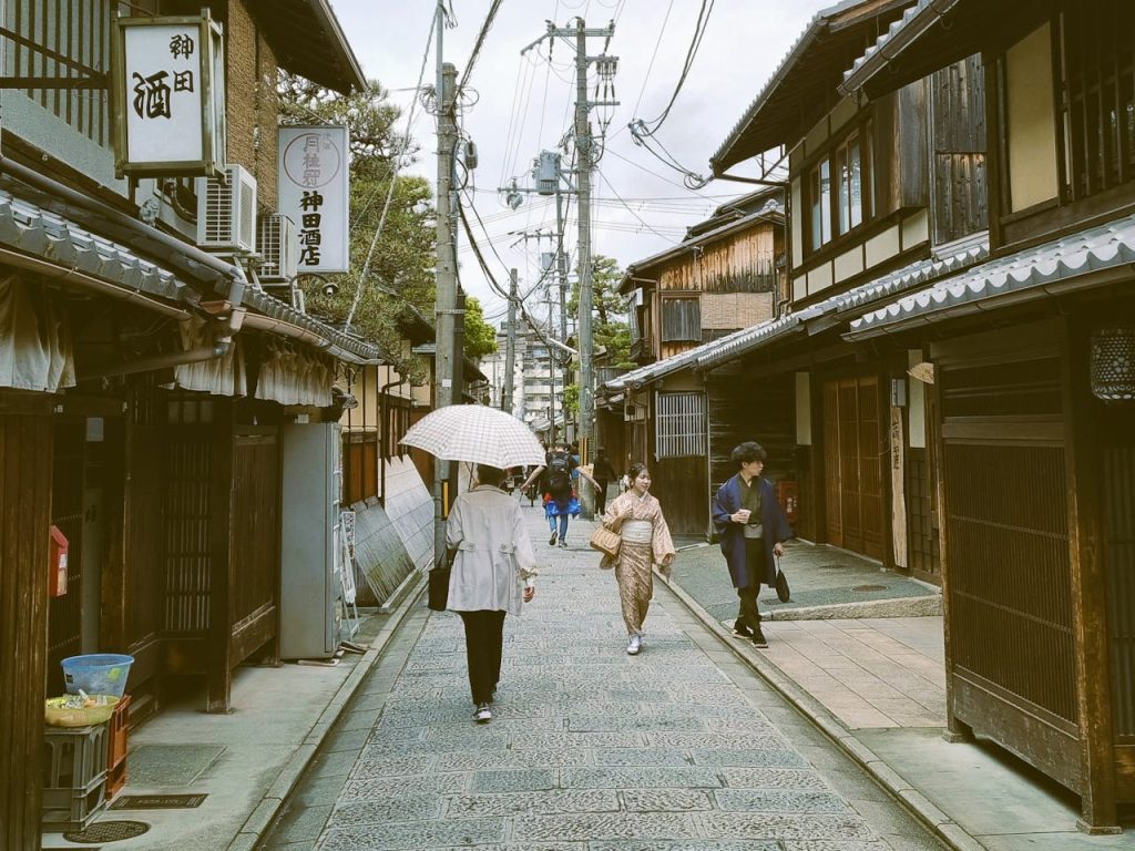 Authentic Kyoto street with people walking under umbrellas amidst traditional Japanese architecture.